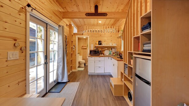 A compact wooden cabin with a kitchen area, a dining table, and a small bathroom. - Modern Lynnwood Tiny House: 16 Mi to Seattle! (Lynnwood)