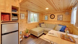 A cozy cabin interior with a wooden ceiling, a sofa, a table, and a refrigerator. - Modern Lynnwood Tiny House: 16 Mi to Seattle! (Lynnwood)