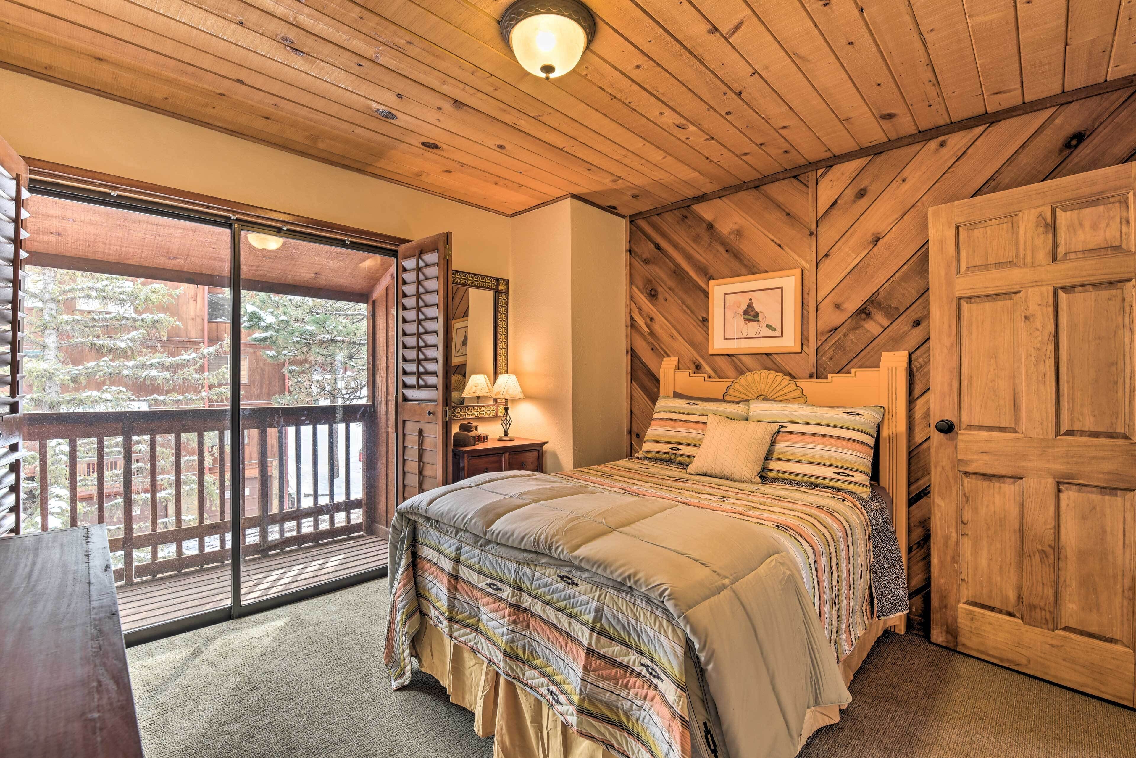 Un dormitorio con una cama grande, techo de madera, puerta corrediza de vidrio a un balcón y una puerta de madera.