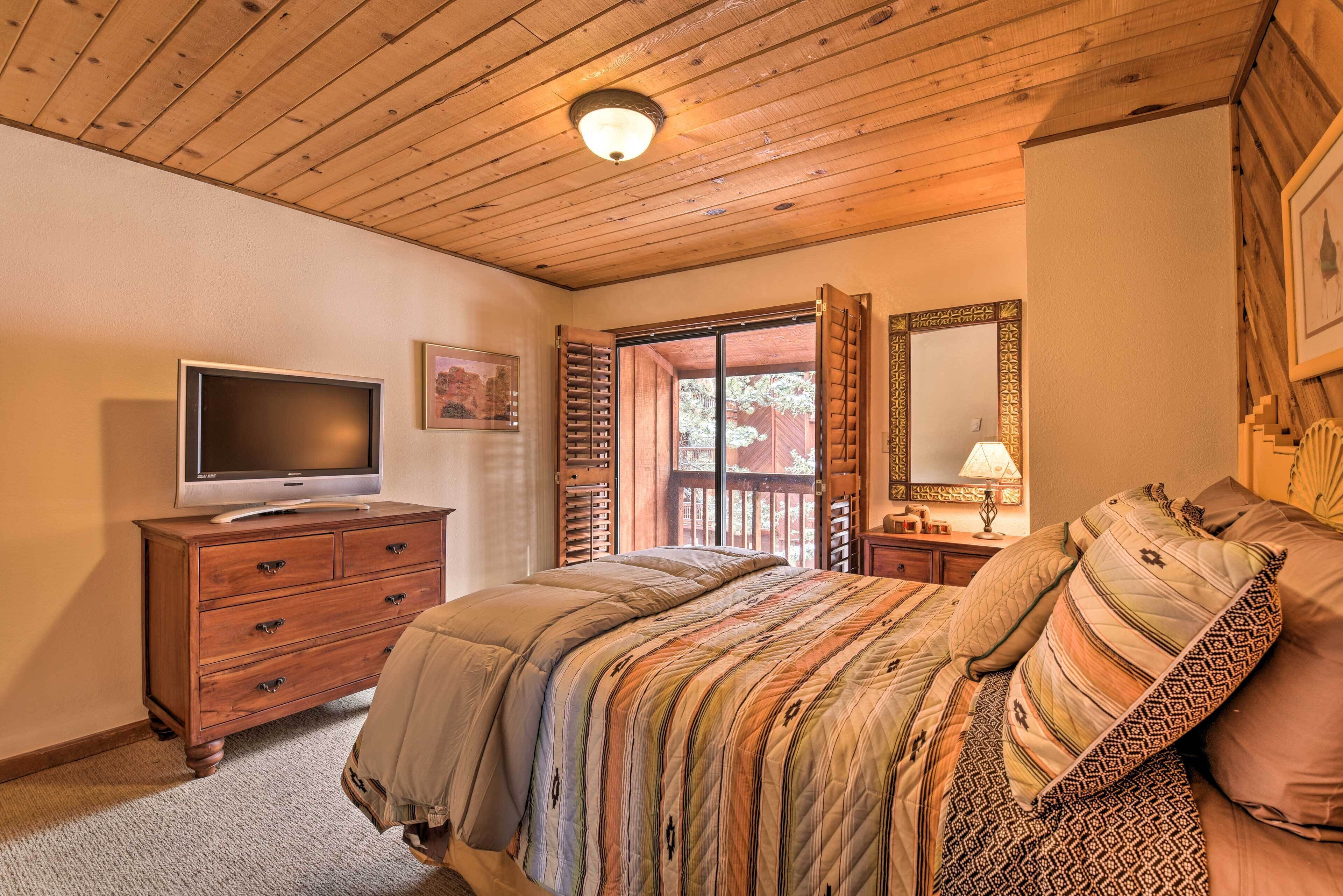 A bedroom with a wooden ceiling, a bed with patterned bedding, a TV on a wooden dresser, and a large mirror.