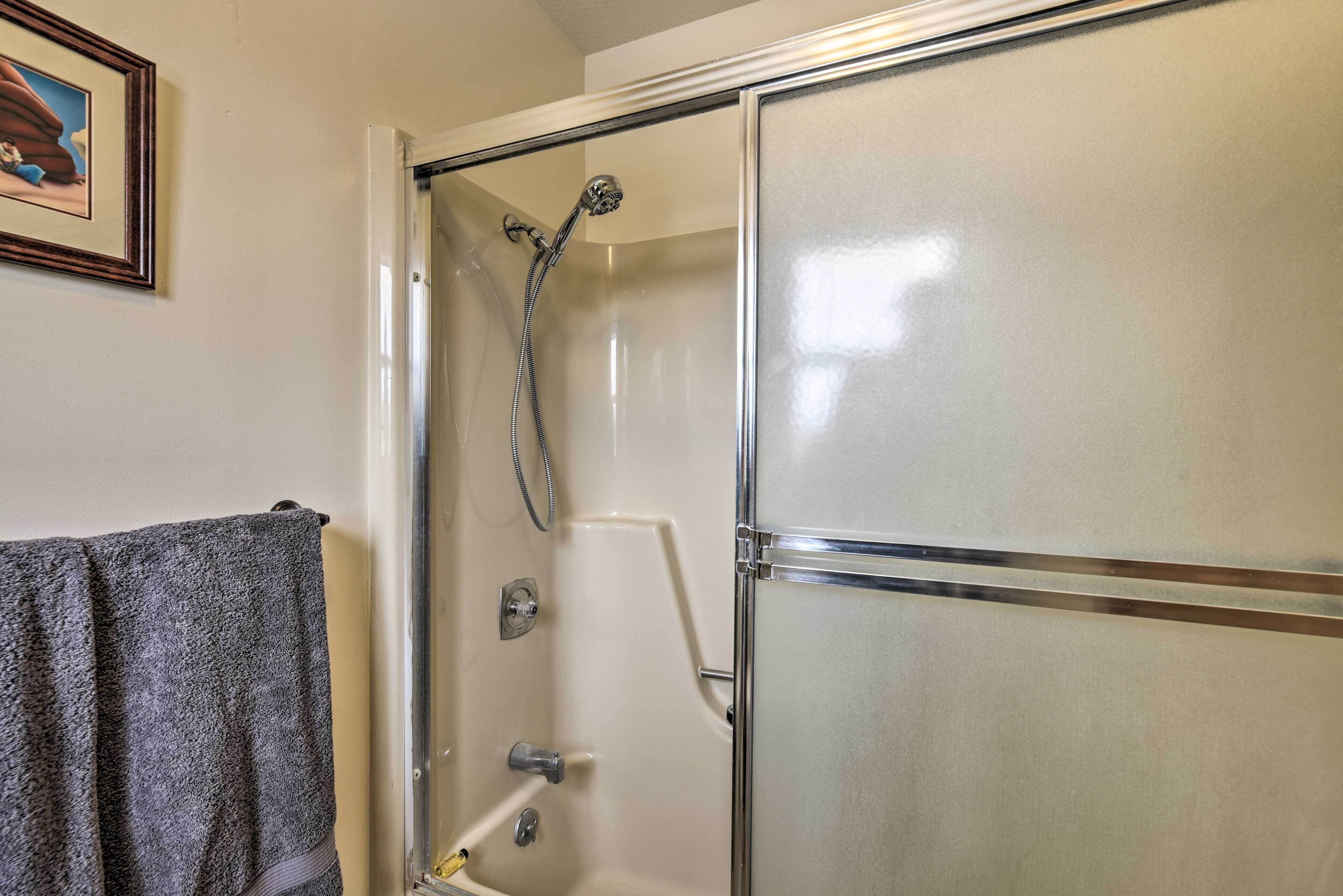Une douche avec une porte en verre, une serviette accrochée au mur et un tableau encadré au-dessus de la serviette.