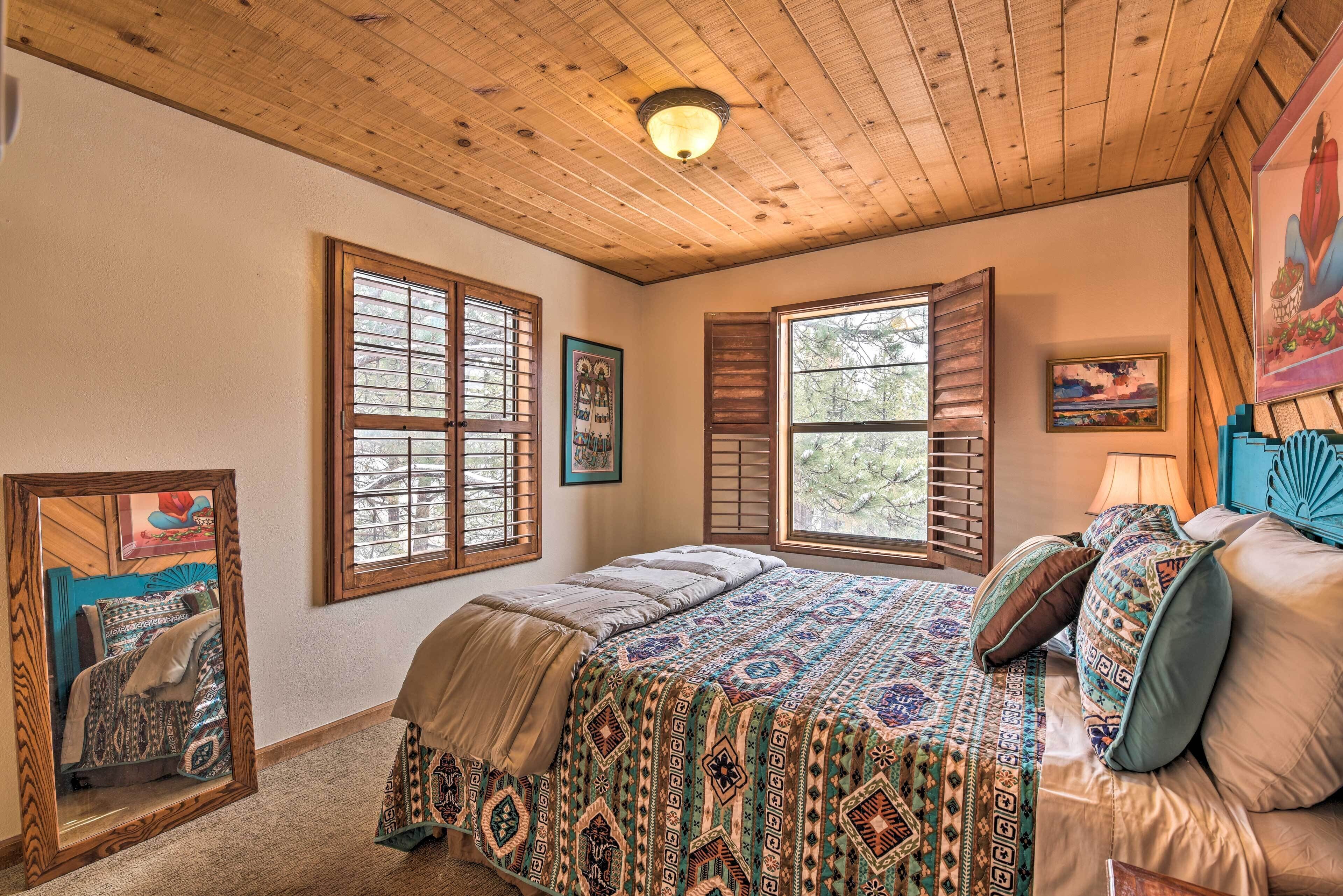 Ein Schlafzimmer mit Holzboden, großen Fenstern, einem Bett mit gemusterten Bettwaren und Bildern an der Wand.