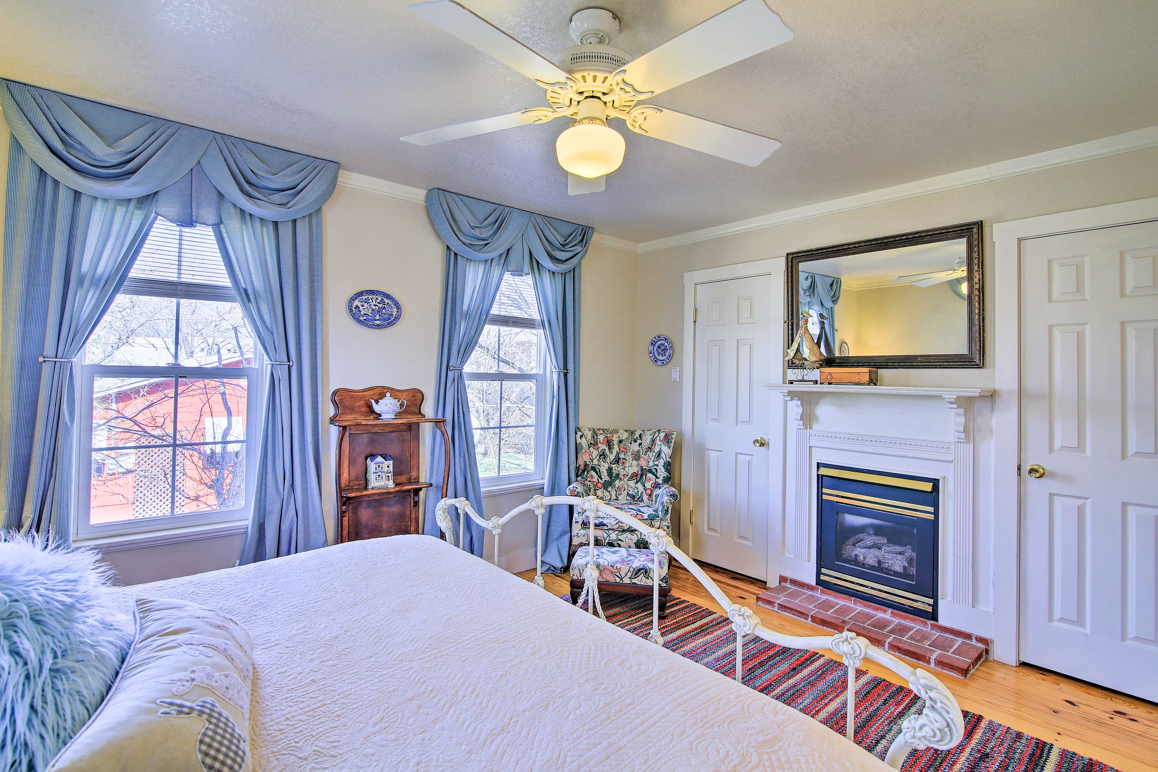 A bedroom with a bed, a ceiling fan, a fireplace, and a chair.