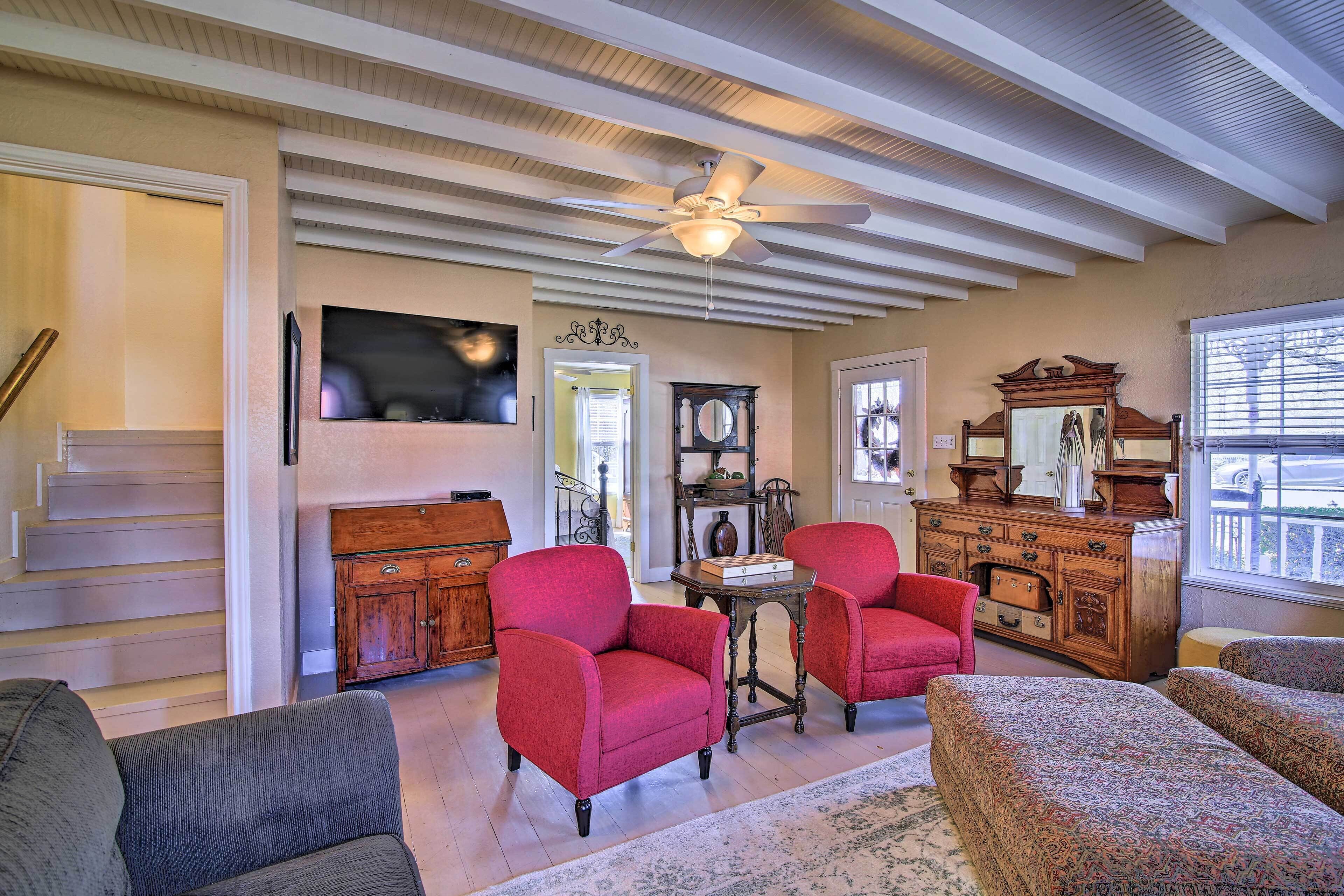 A spacious living room with a high ceiling, a ceiling fan, and a large window.