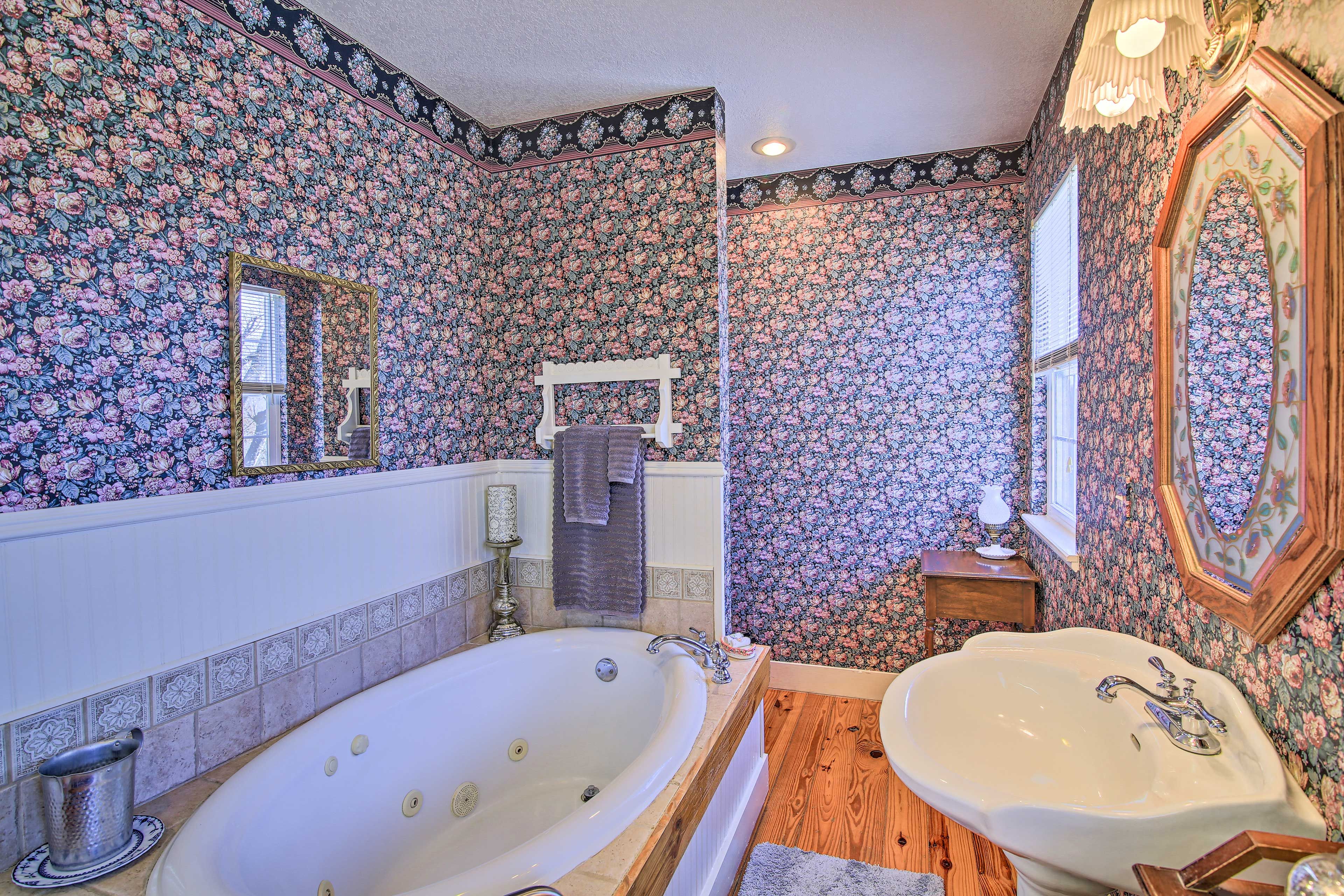 A bathroom with floral wallpaper, a freestanding bathtub, a sink, and a mirror.