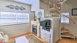 A cozy living room with a fireplace, a TV, a staircase, and a window with blinds. - Walk to Main St: Multiple Fireplaces, Jacuzzi Tubs (Fredericksburg)