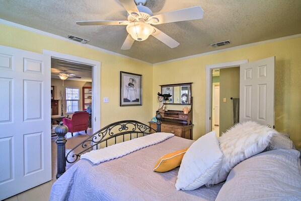 A bedroom with a bed, a ceiling fan, a dresser, a mirror, and a door leading to another room. - Hist District/walk to Main/jacuzzi Tubs/fireplaces (Fredericksburg)