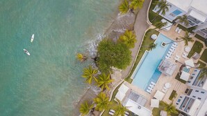 Vista aerea di un hotel sulla costa con piscina, spiaggia e palme.