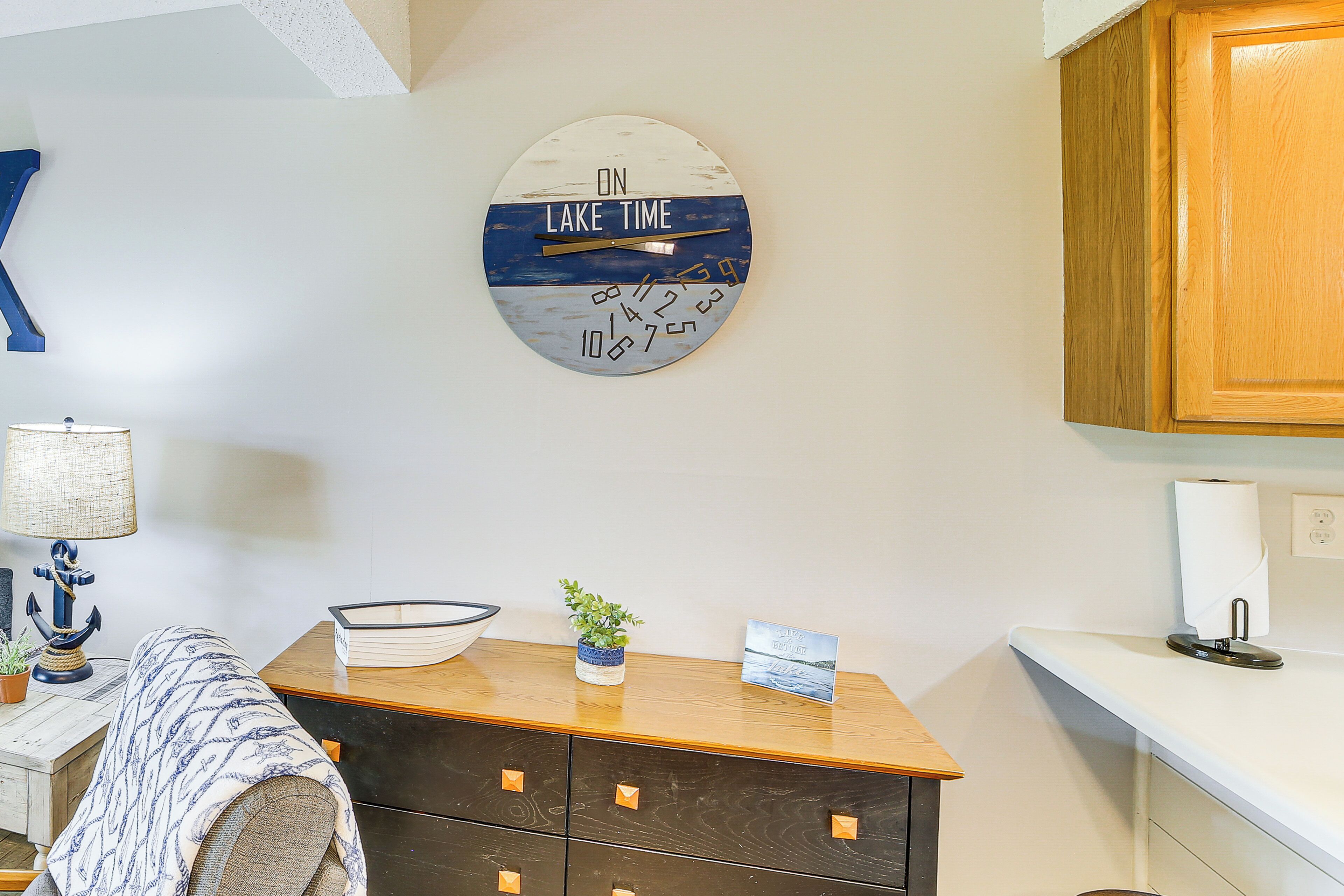 A room with a wooden dresser, a wall clock, a lamp, and a small plant.