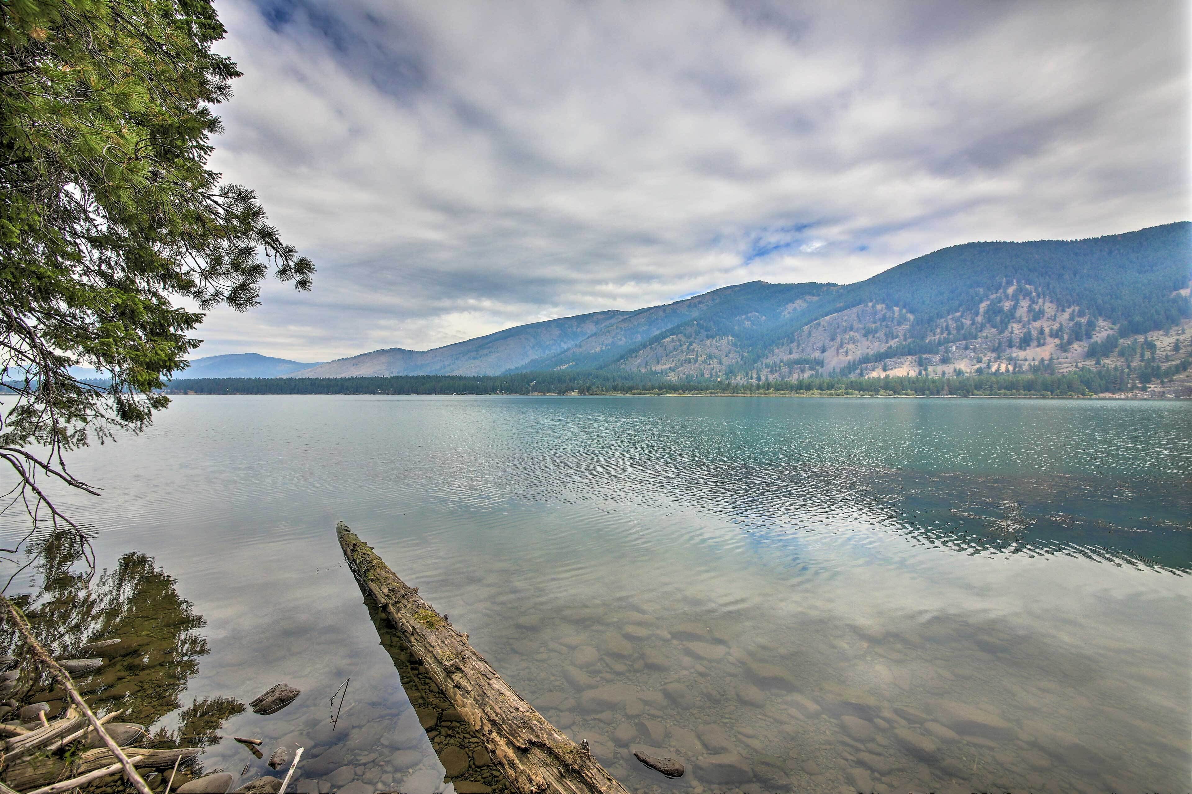 A calm lake with clear water, surrounded by mountains and trees.