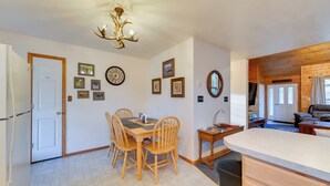 A dining area with a wooden table and chairs, a chandelier, and wall-mounted clocks and pictures.