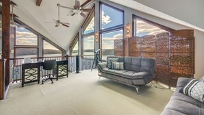Ein geräumiges Schlafzimmer im Loft-Stil mit großen Fenstern, Deckenventilator, Schreibtisch und einer Couch.