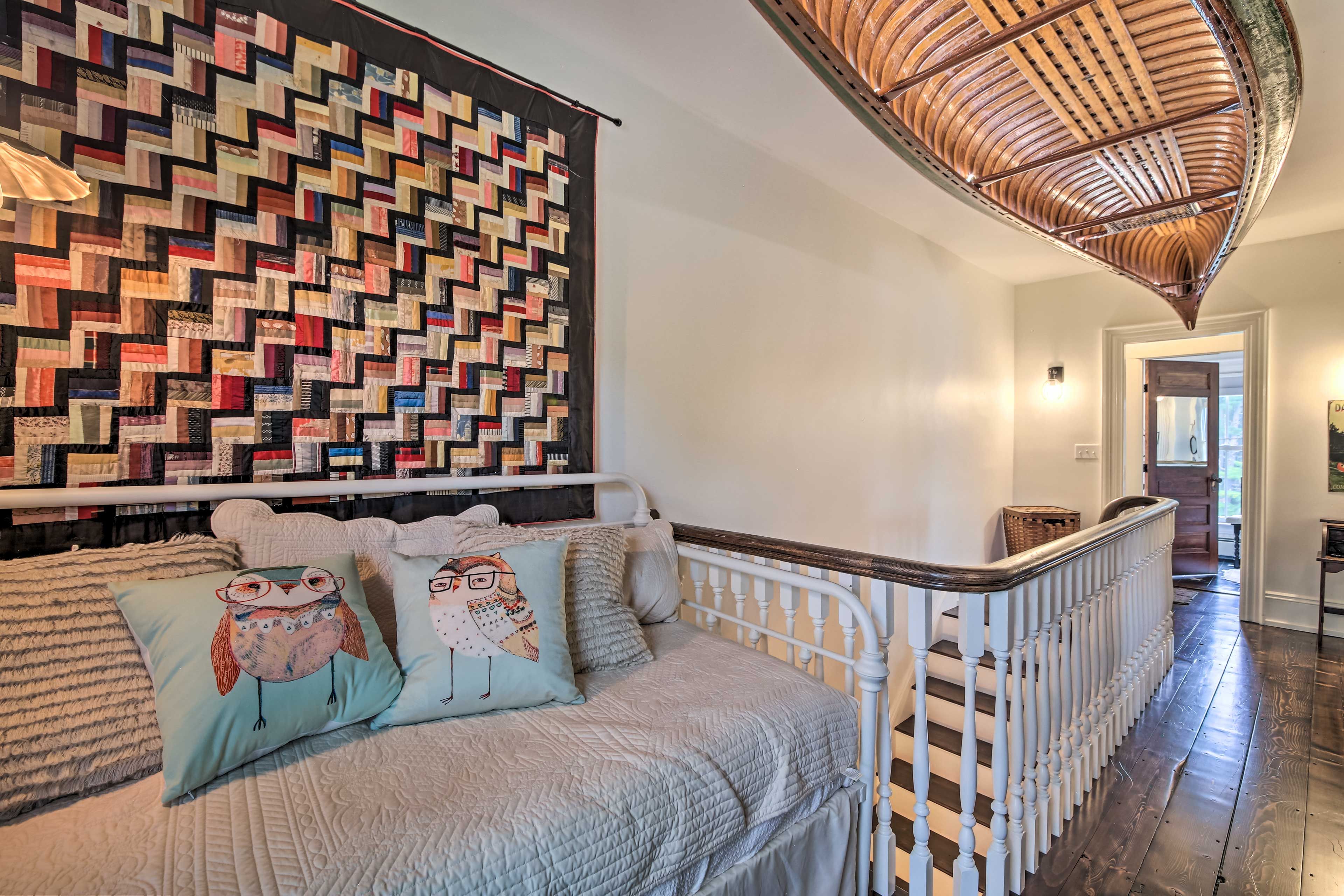 A cozy room with a quilted sofa, a wooden ceiling, and a staircase.
