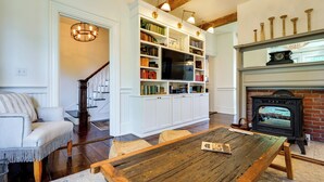 A cozy living room with a fireplace, a wooden dining table, a sofa, and a bookshelf filled with books. - On-site Pond: Spacious Family Home in Jefferson! (Jefferson)
