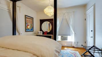 A bedroom with a large bed, a chandelier, a framed poster, a mirror, and a window with curtains.