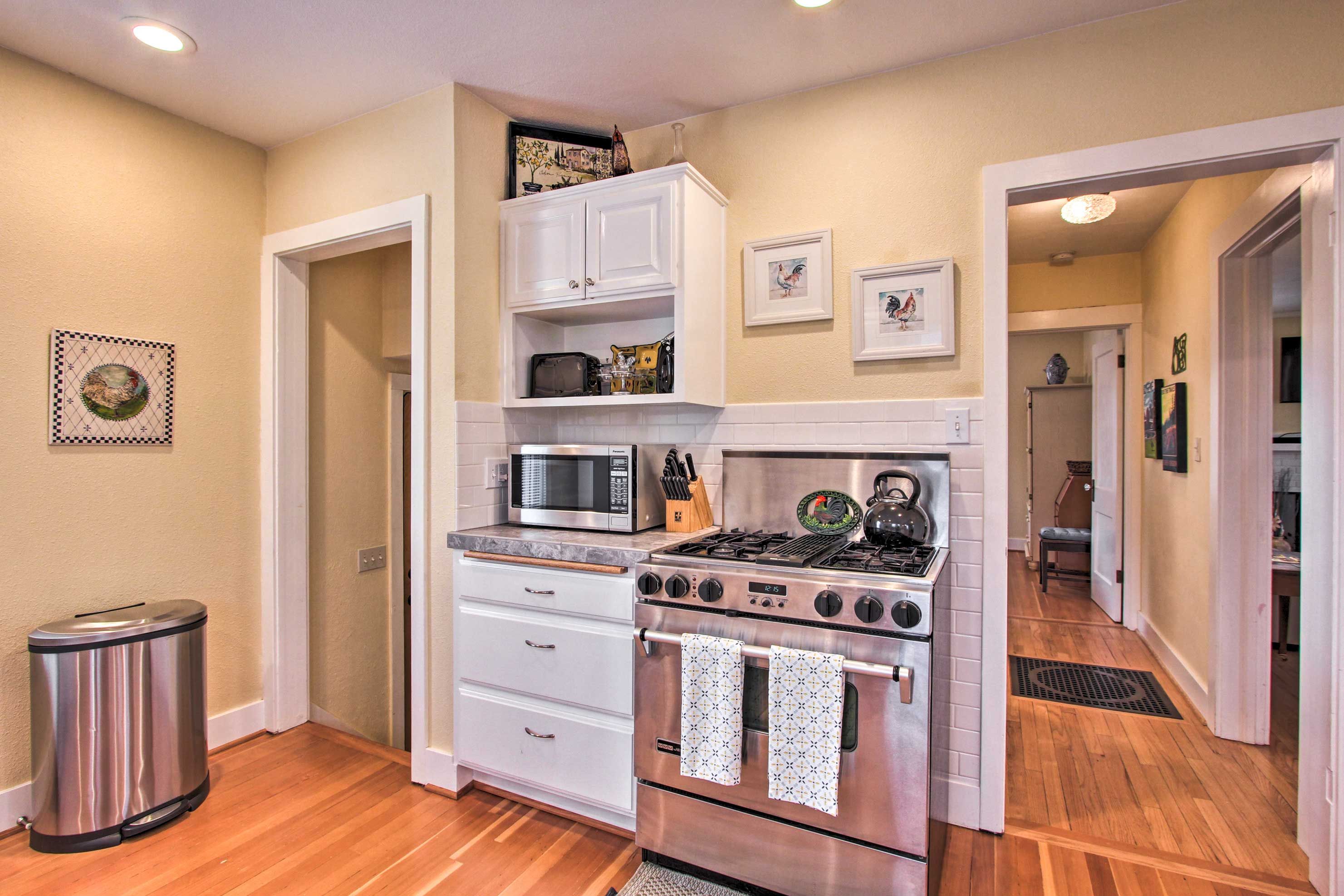 A kitchen with white cabinets, a stainless steel stove, a microwave, and a trash can.
