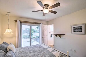 A bedroom with a bed, a ceiling fan, a window with curtains, a door, and a wall-mounted shelf. - Pet-friendly Sebastian Home on Lake; Golf Nearby (Sebastian)