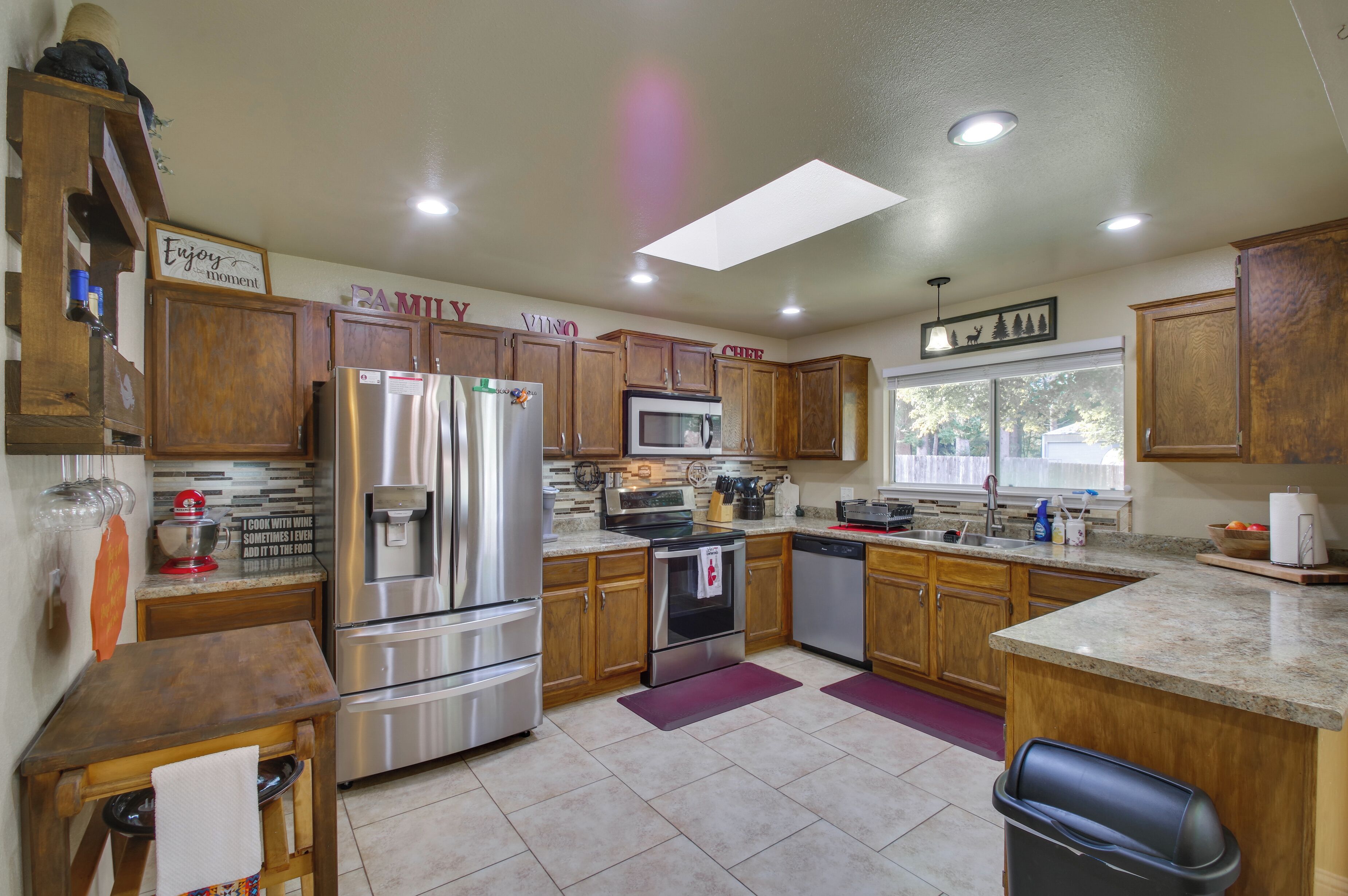 A kitchen with wooden cabinets, stainless steel appliances, a granite countertop, and a window with a view of trees.