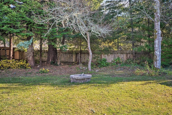 A backyard with a wooden fence, a stone fire pit, and various trees.