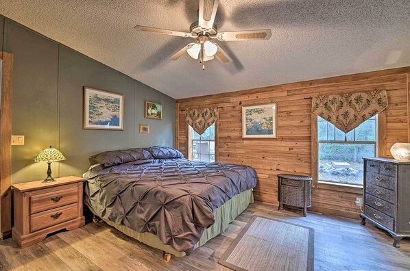 A bedroom with a bed, wooden walls, a ceiling fan, a nightstand, a dresser, and framed pictures on the wall. - 13 Mi to Silver Springs: Pet Friendly Getaway! (Silver Springs)