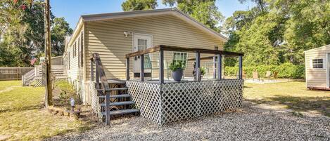 A single-story mobile home with a covered porch, a small outdoor seating area, and a gravel driveway.