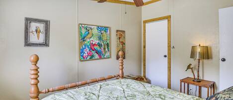Een slaapkamer met een houten bedframe, een plafondventilator en kunstwerken aan de muren.