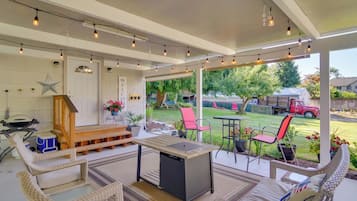 A covered patio area with a table and chairs, a fire pit, and a view of a backyard with a lawn and a red truck.