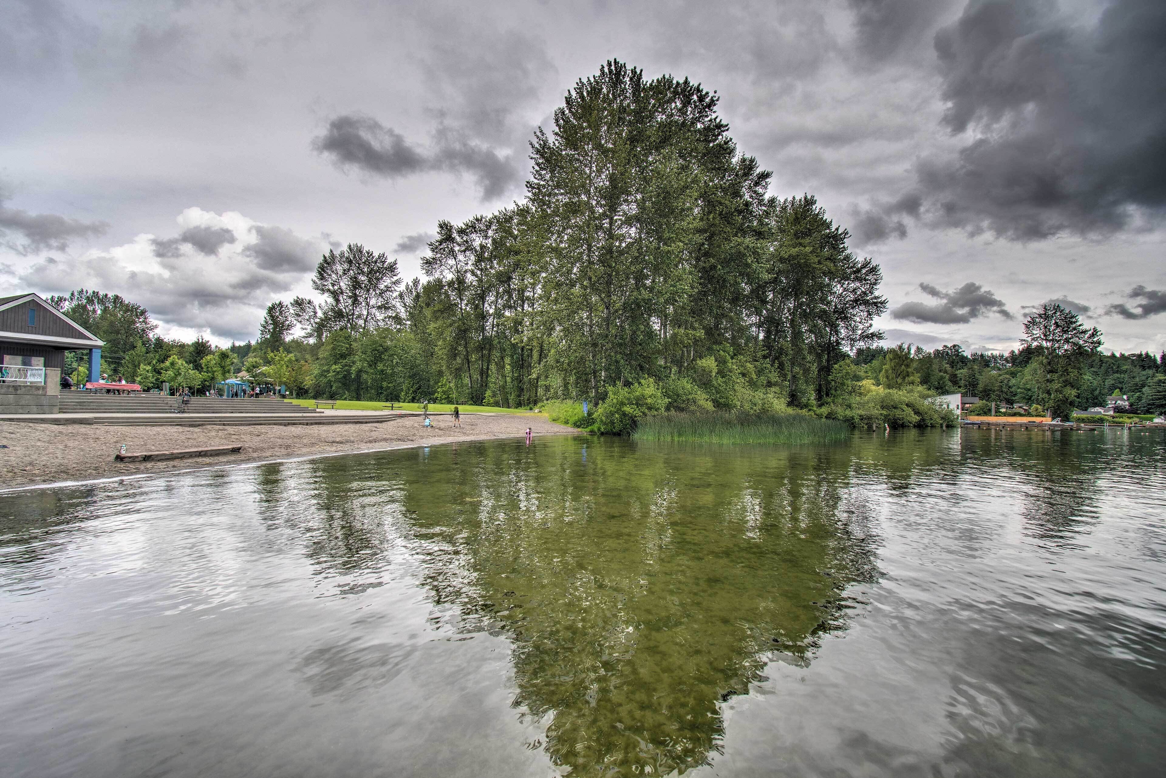 A lakeside view with a dock, a building with a blue roof, and a large tree in the background.