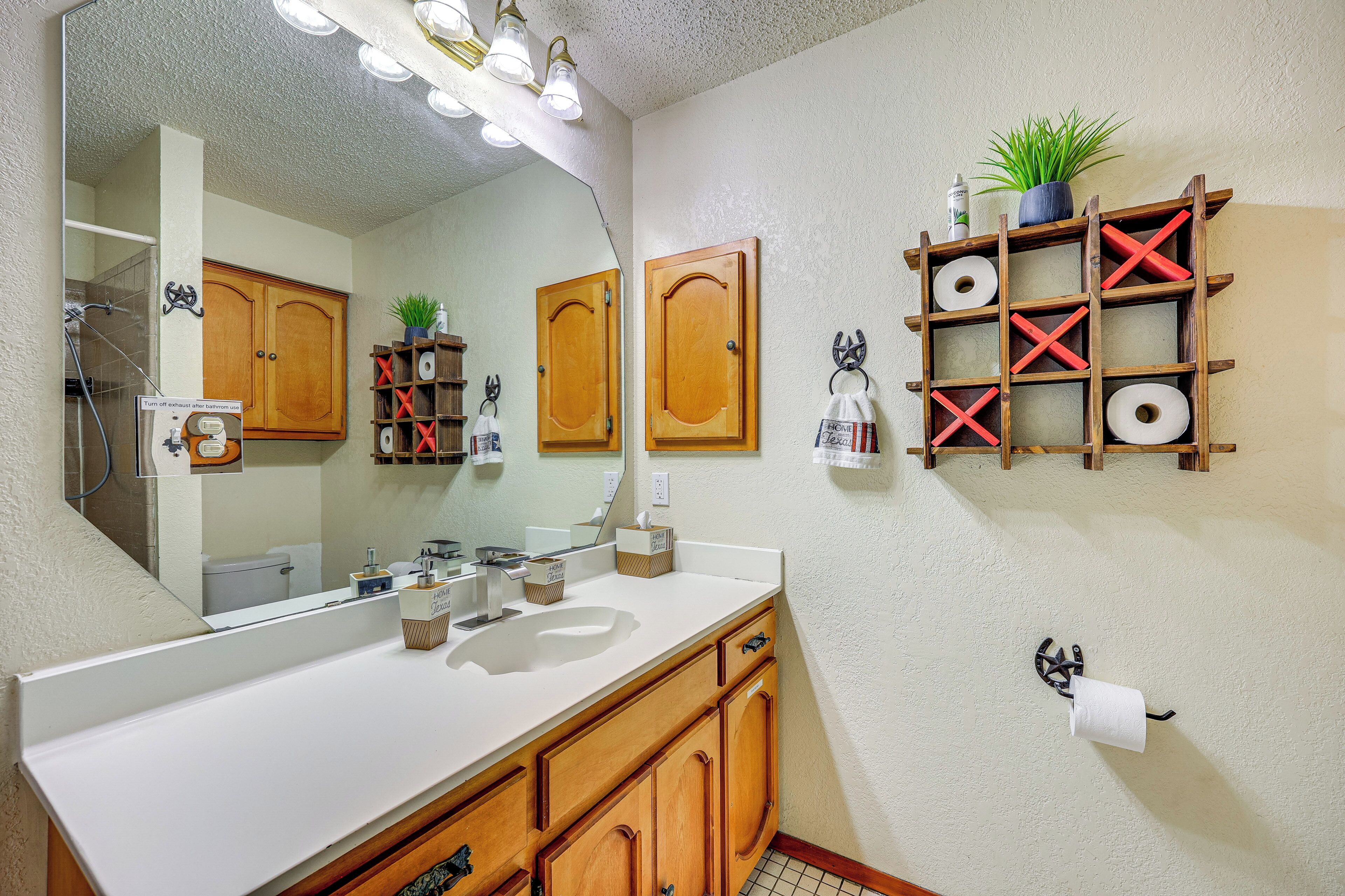 A bathroom with a large mirror, wooden cabinets, a sink, and a shelf with toiletries.