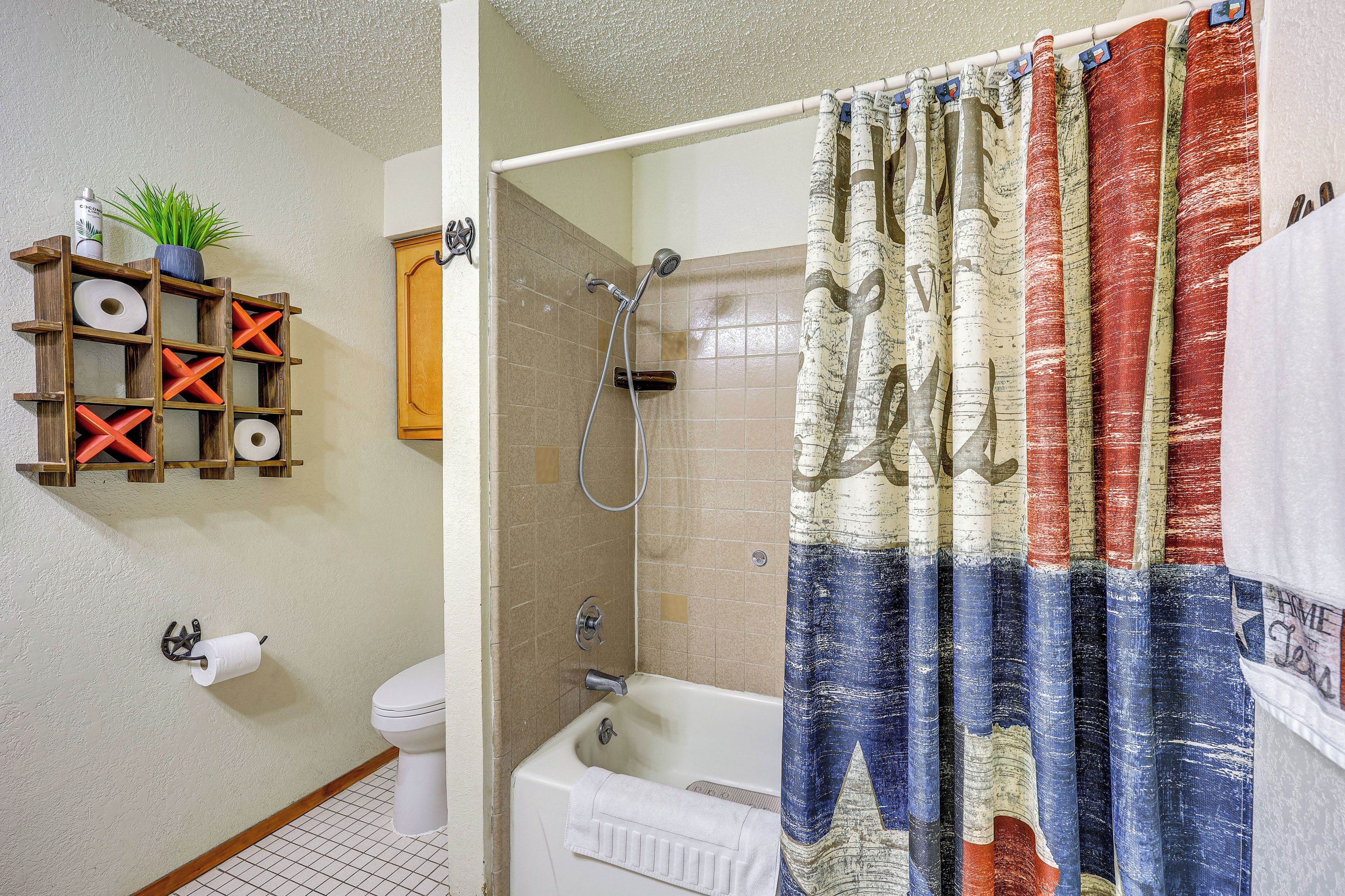 A bathroom with a shower curtain, toilet, and a shelf with toiletries.