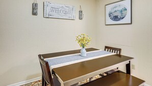 A dining area with a wooden table, a vase with yellow flowers, and wall decorations including a 'WELCOME' sign and a framed picture. - Relaxing Helotes Apt: 7 Mi to UT at San Antonio! (Helotes)