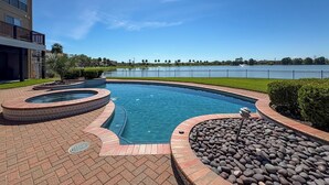 A swimming pool with a hot tub, surrounded by a brick patio and a stone border. - Lakefront Houston House - 1 Mi to Space Center! (Houston)