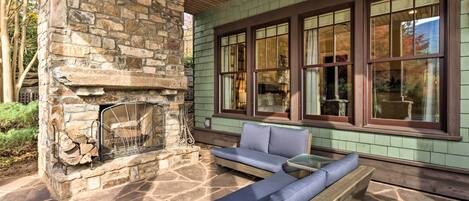 A stone fireplace with a fire, a wooden bench, and a table with blue cushions.