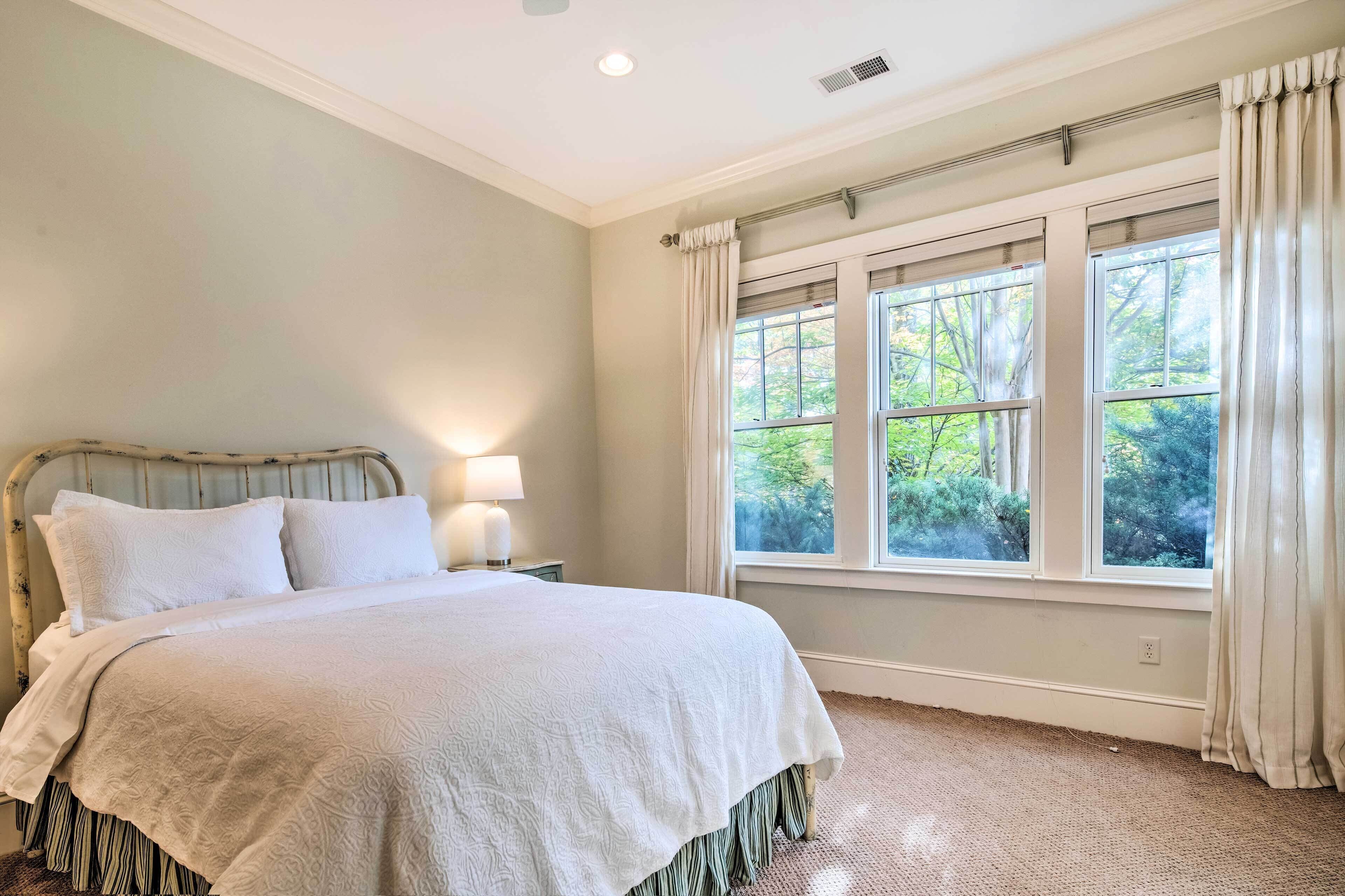 A bedroom with a large bed, a nightstand with a lamp, and a window with curtains.