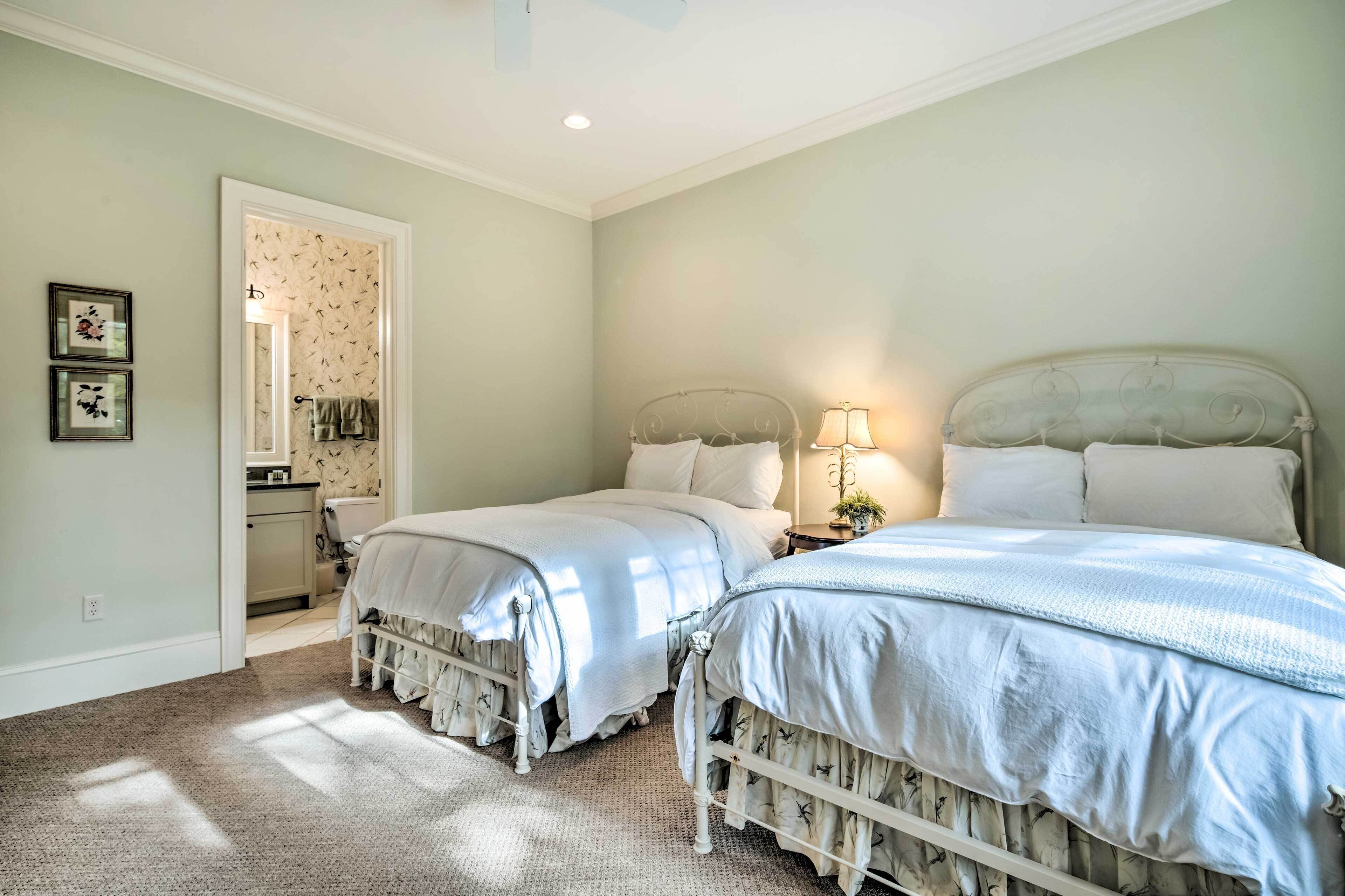 A bedroom with two beds, a nightstand with a lamp, and a bathroom visible through an open door.