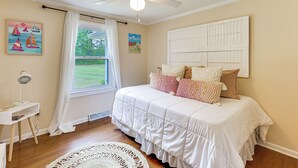 Een slaapkamer met een bed, een plafondventilator, een raam met gordijnen en kunstwerken aan de muur.