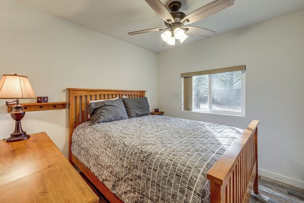 A bedroom with a wooden bed, a nightstand, a lamp, and a window. - Kalispell Cabin 28 Miles to Glacier National Park! (Kalispell)