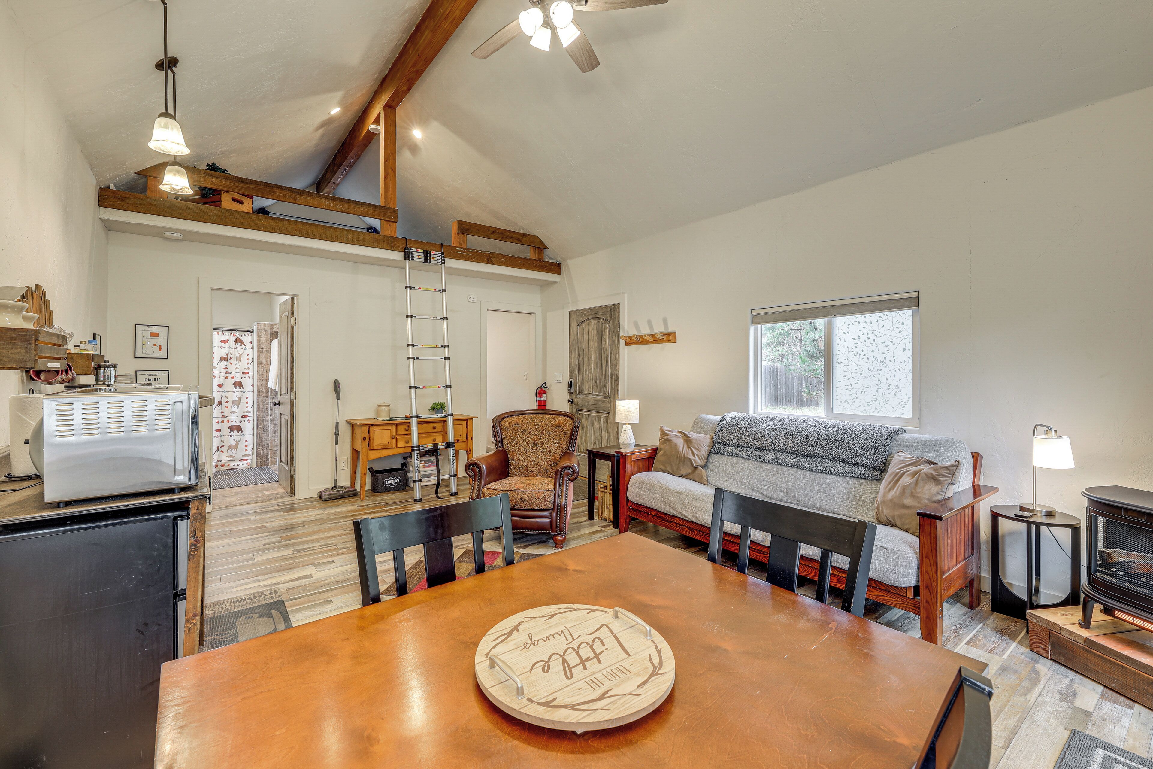 A cozy living room with a wooden dining table, a sofa, a fireplace, and a ladder leading to a loft space.