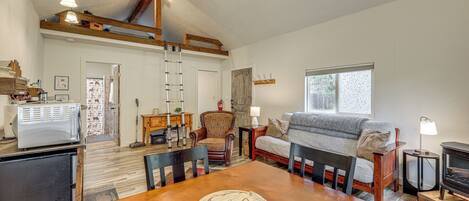 A cozy living room with a wooden dining table, a sofa, a fireplace, and a ladder leading to a loft space.