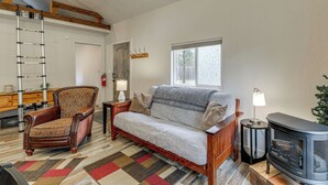 A cozy living room with a wooden sofa, a patterned armchair, a fireplace, and a ladder against the wall. - Kalispell Cabin 28 Miles to Glacier National Park! (Kalispell)