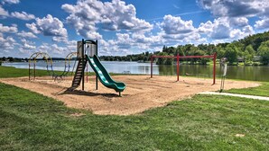 A playground with a slide and swings, a lake in the background, and a clear sky. - Guilford Lake Cottage w/ Hot Tub & Water Views (Lisbon)
