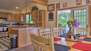 A kitchen with wooden cabinets, a central island, and a dining area with chairs and a table. - Guilford Lake Cottage w/ Hot Tub & Water Views (Lisbon)