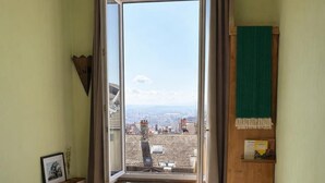 A bedroom with a bed, a radiator, a window with curtains, and a view of buildings. - Charming croix roussien apartment Lyon 1 (THIZY LES BOURGS)