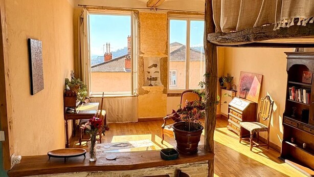 A cozy room with a wooden dining table, chairs, a bookshelf, a potted plant, and a view of the outside. - Charming croix roussien apartment Lyon 1 (THIZY LES BOURGS)
