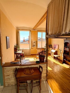 Une pièce chaleureuse avec une table à manger en bois, des chaises, une bibliothèque, une plante en pot et une vue sur l’extérieur.