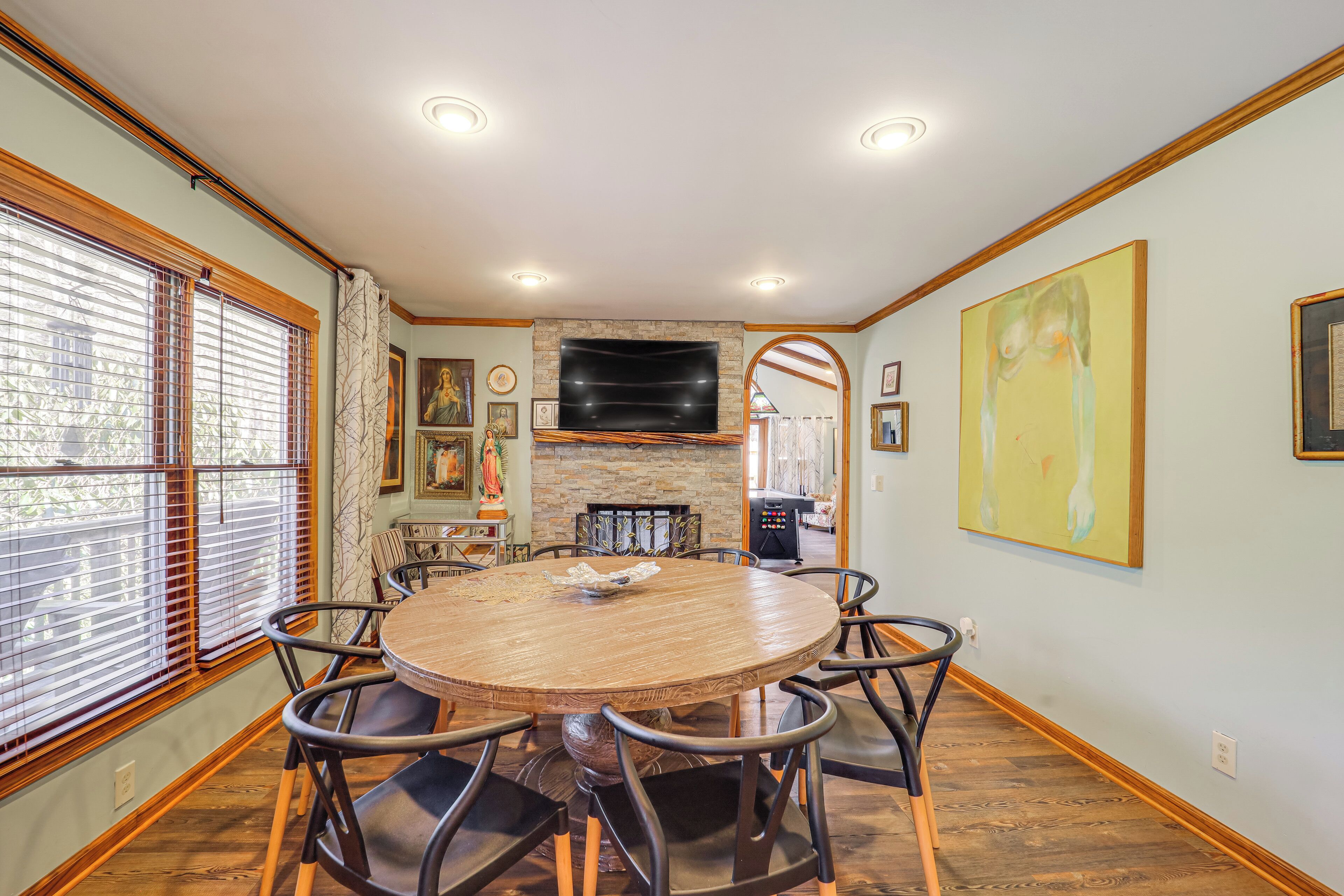 A dining area with a round wooden table, black chairs, a stone fireplace, and artwork on the walls.