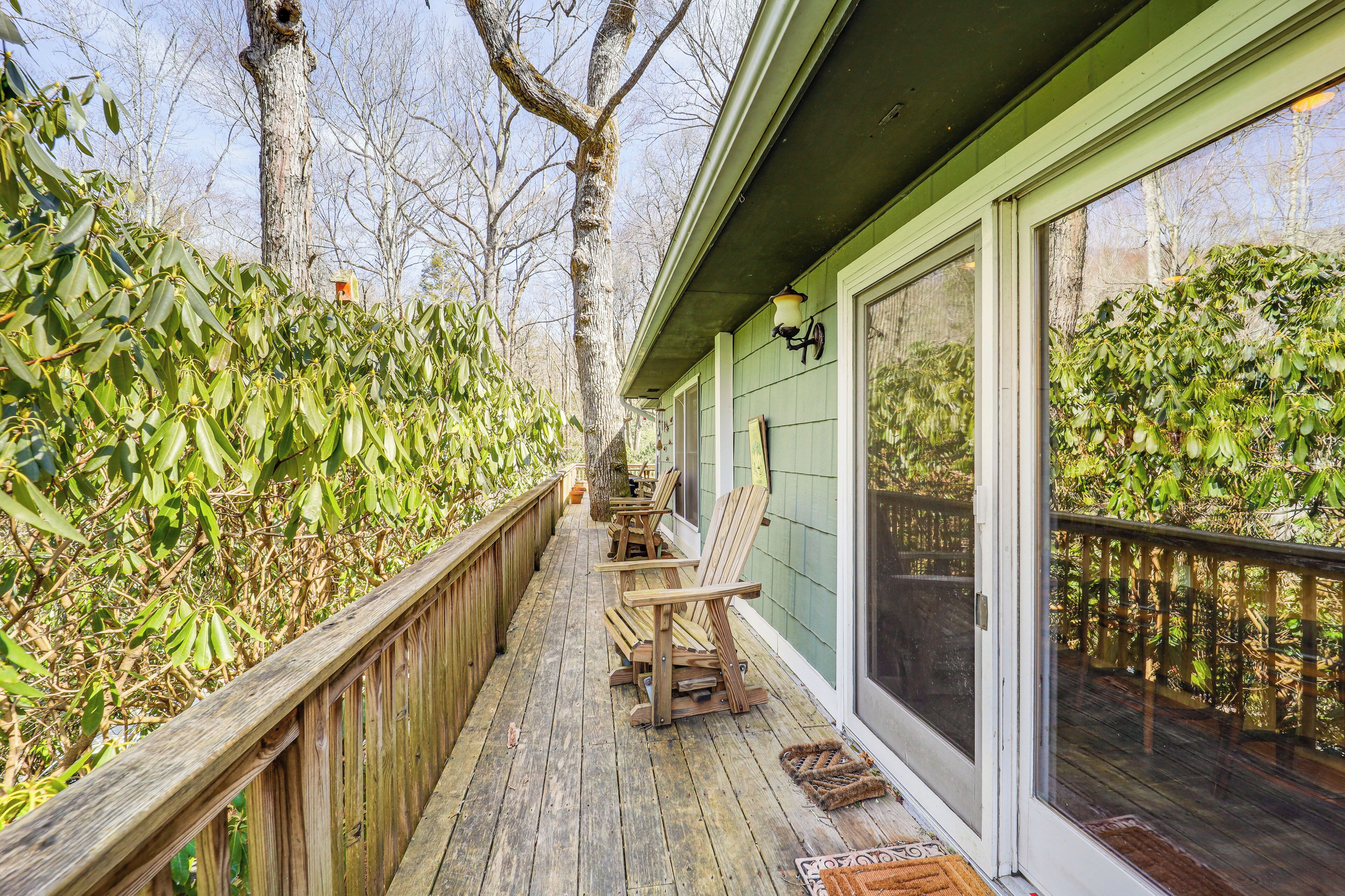 A wooden deck with chairs, a wooden railing, and a glass door leading to a covered area.