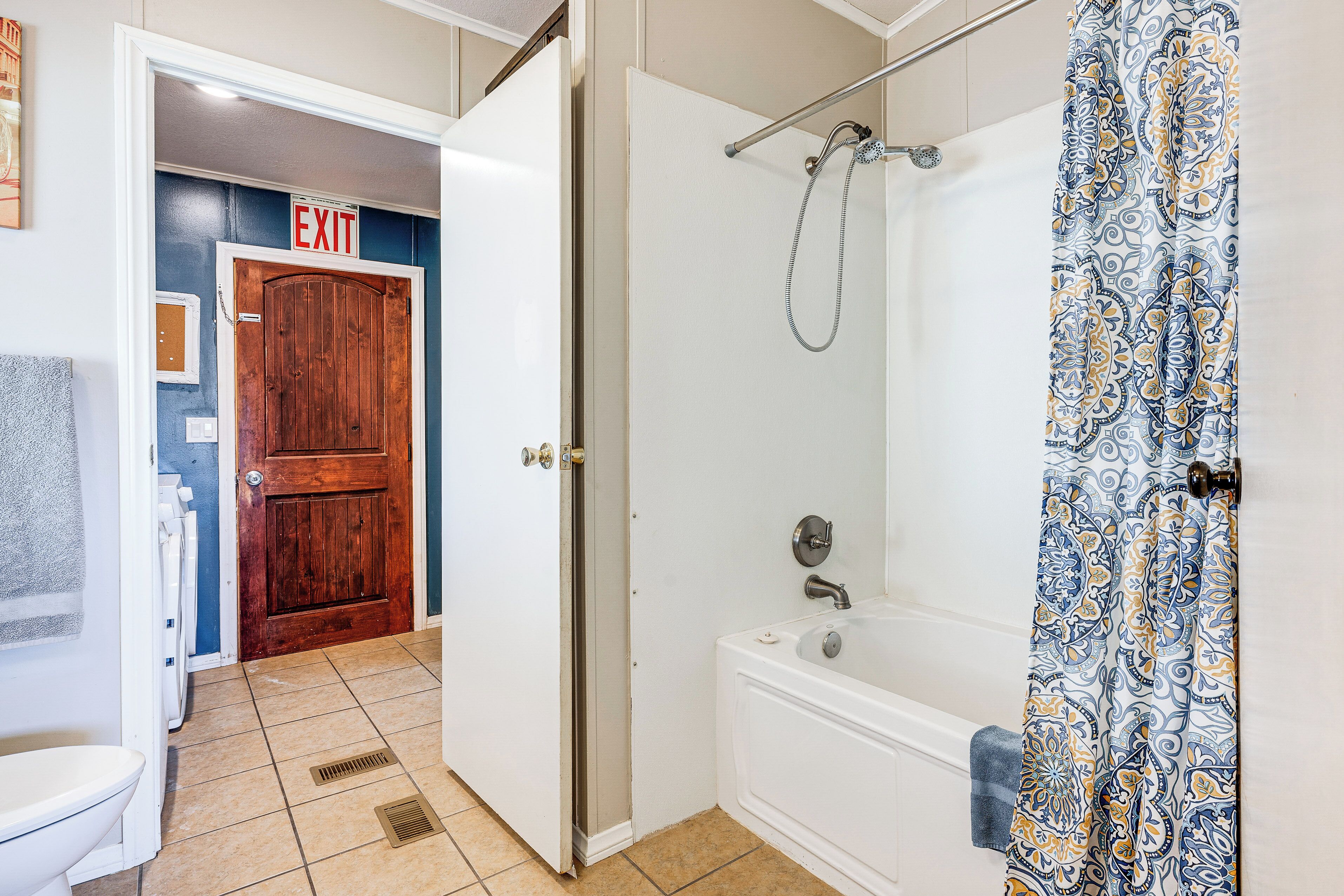 Baño con bañera, ducha y puerta de salida.