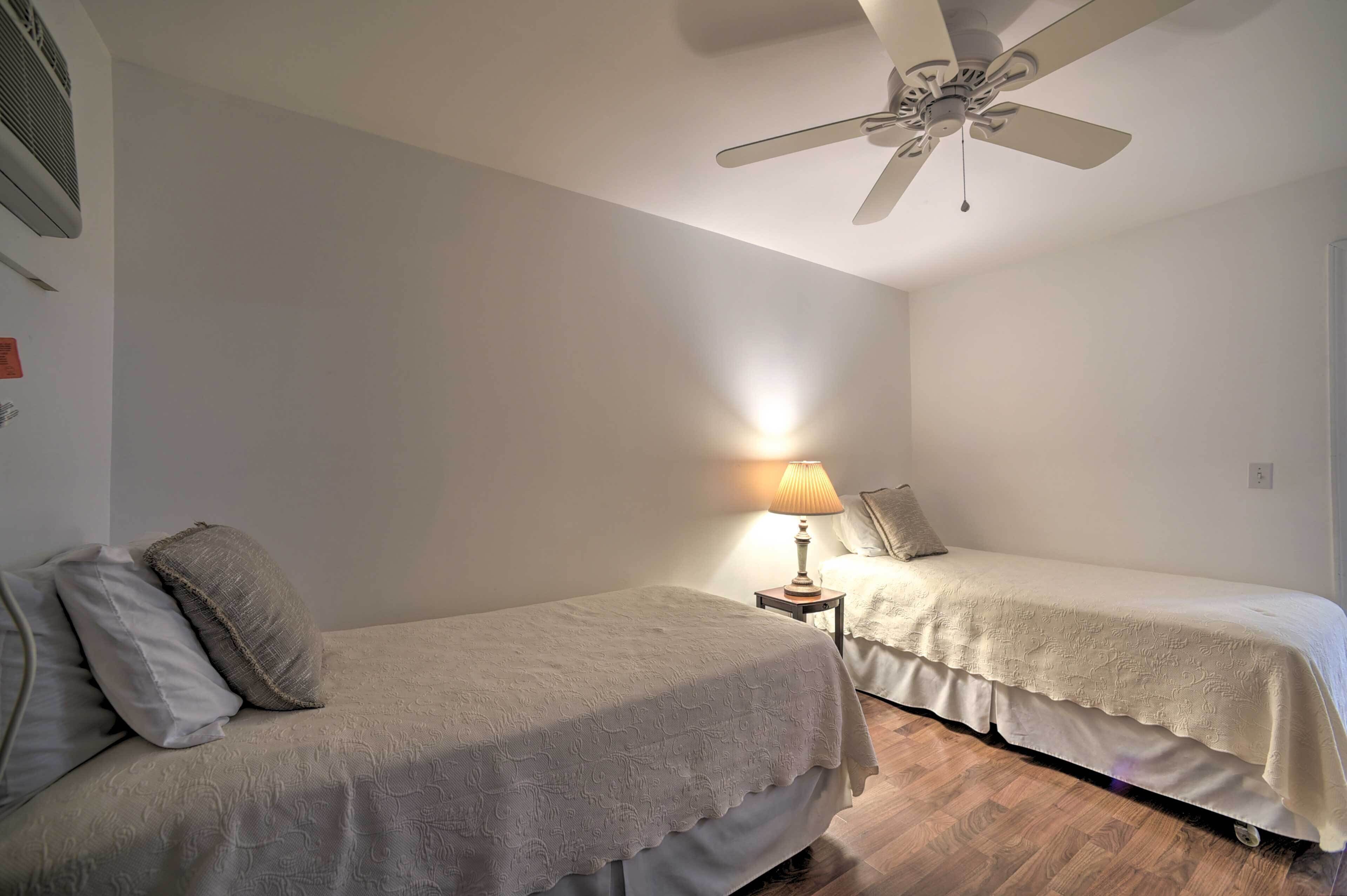 Ein Schlafzimmer mit zwei Einzelbetten, einem Deckenventilator, einer Nachttischlampe und einer Klimaanlage.