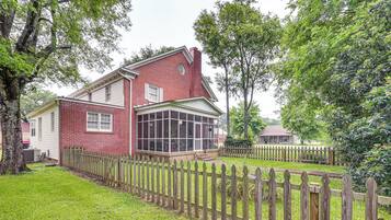 A two-story house with a large glass windowed porch, surrounded by a wooden fence and lush greenery.